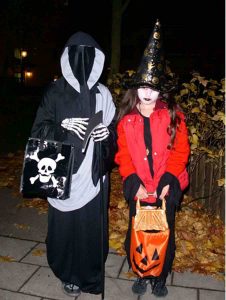 A picture of two trick-or-treaters. One is dressed as a faceless specter, the other as a witch.