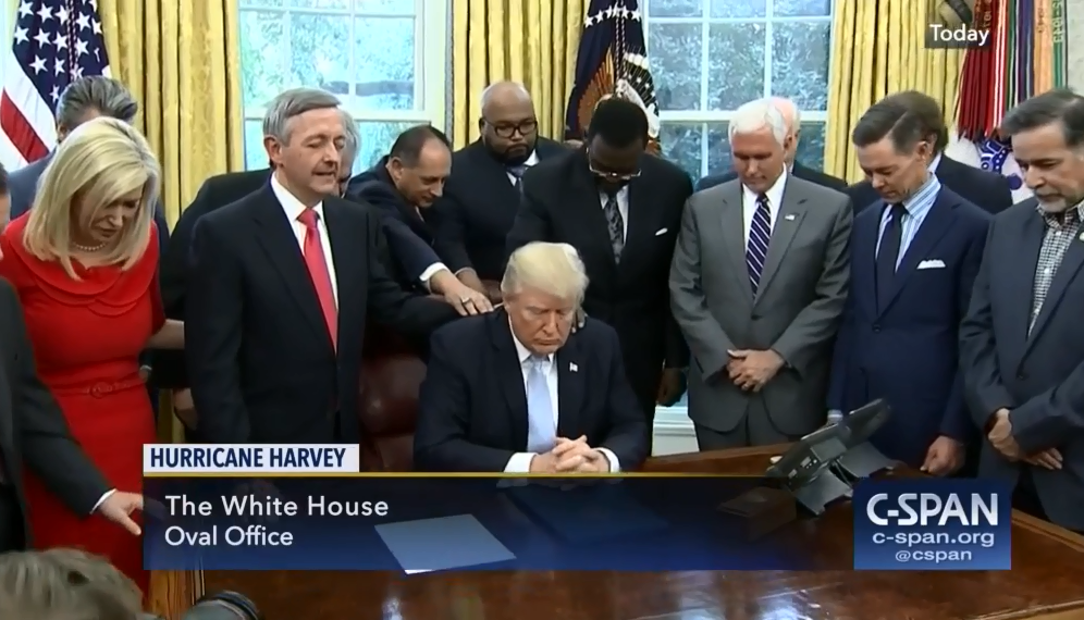 Former U.S. President Donald Trump, surrounded by former Vice-President Mike Pence, and about a dozen Evangelical leaders who are praying over him.